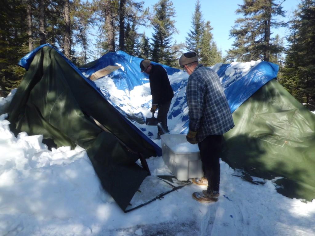 Two men contemplating a tent buried under snow.
