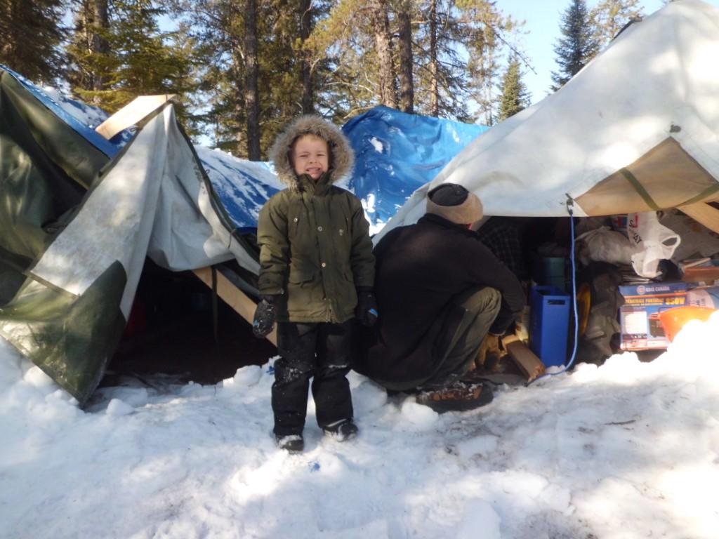 Young boy smiling beside collapsed tent in winter.