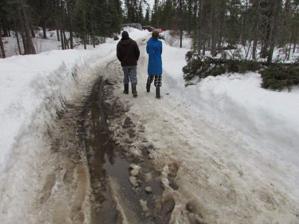 Two men walking up a muddy and snowy driveway.