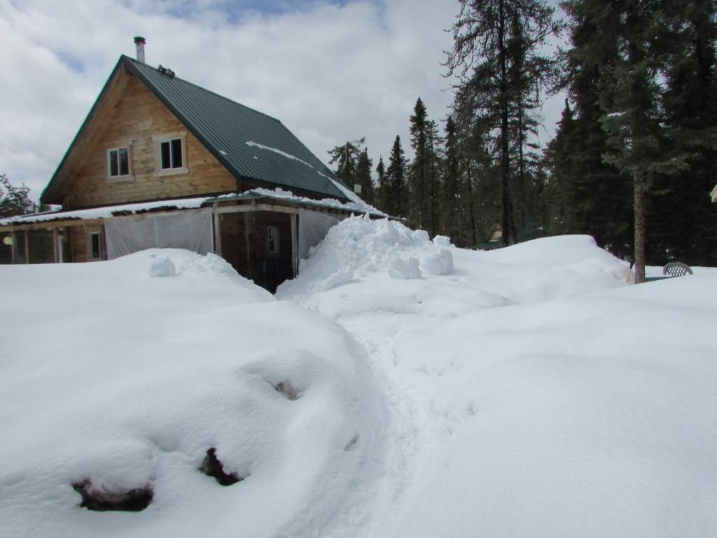 Snow piled up the the porch roof of a log cabin.