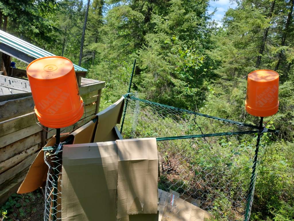 Makeshift fence with cardboard walls and bright orange buckets draped from the corners.