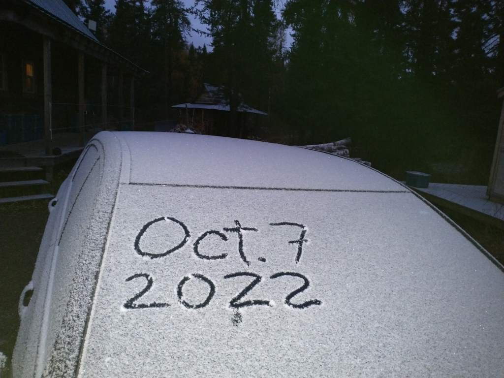 A car windscreen covered in snow with the date Oct. 7 2022 written in finger.