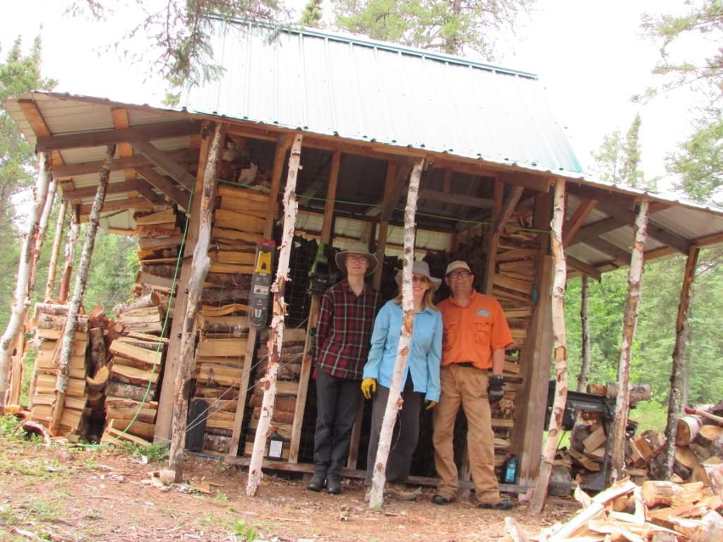 A happy family in front of a half full woodshed.